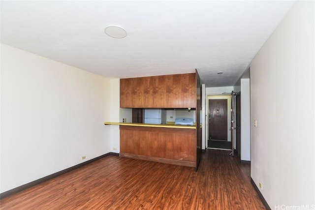 kitchen featuring dark wood-type flooring, baseboards, light countertops, a peninsula, and brown cabinetry