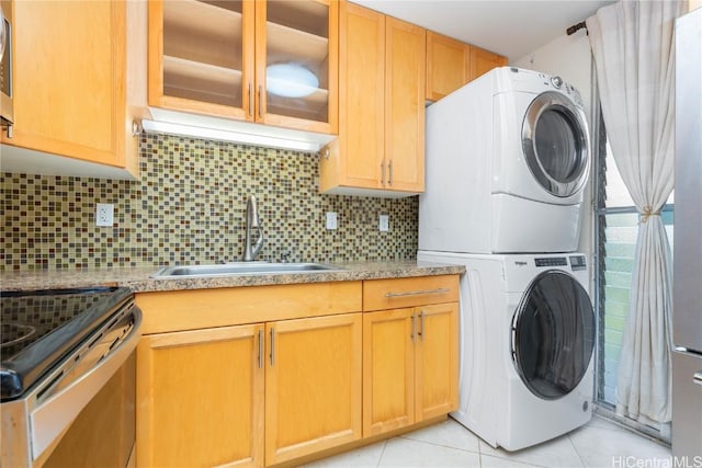 laundry area featuring stacked washer and clothes dryer, light tile patterned floors, a sink, and laundry area