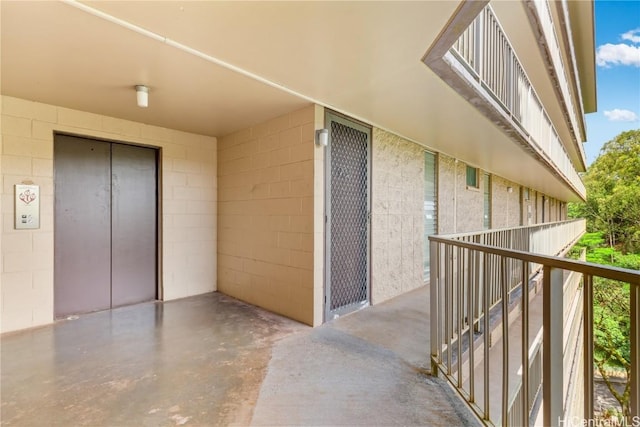 entrance to property with concrete block siding, elevator, and a balcony