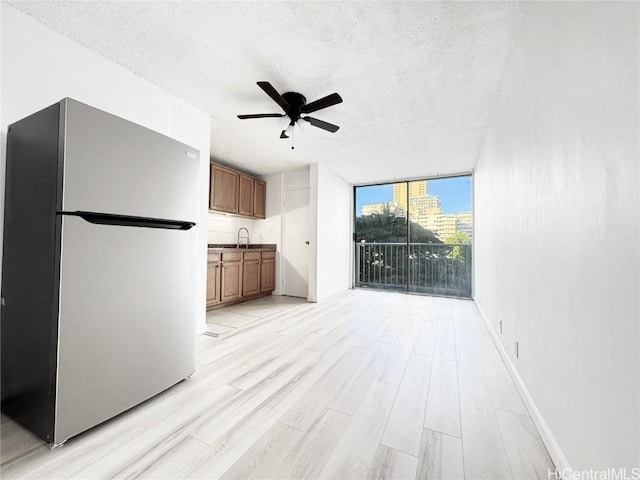 kitchen with brown cabinets, a ceiling fan, freestanding refrigerator, expansive windows, and light wood-type flooring