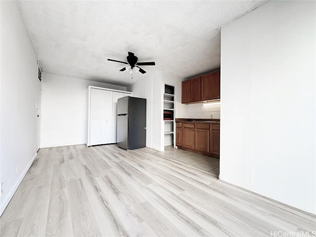 unfurnished living room featuring a ceiling fan, light wood-type flooring, and a textured ceiling