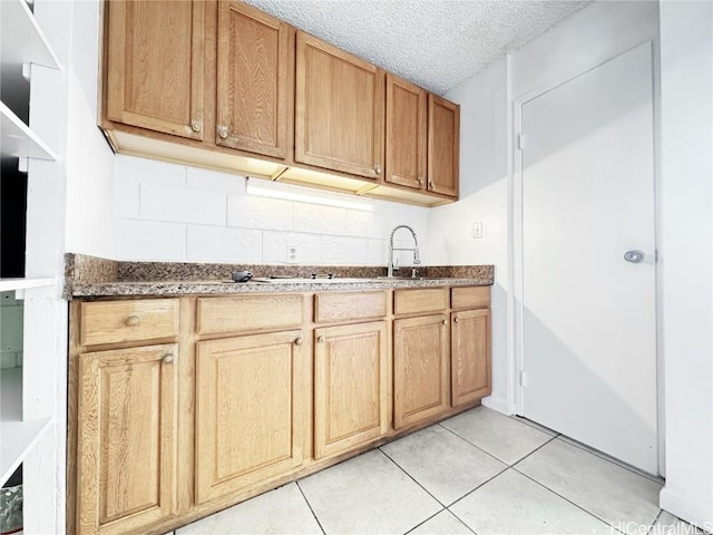 kitchen featuring tasteful backsplash, light tile patterned flooring, a sink, and a textured ceiling