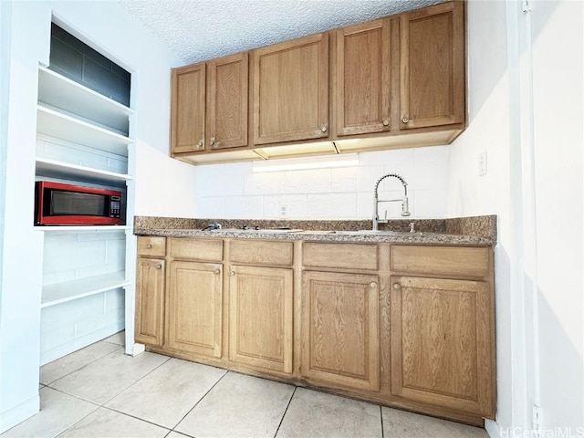 kitchen featuring dark stone countertops, a sink, built in microwave, a textured ceiling, and backsplash