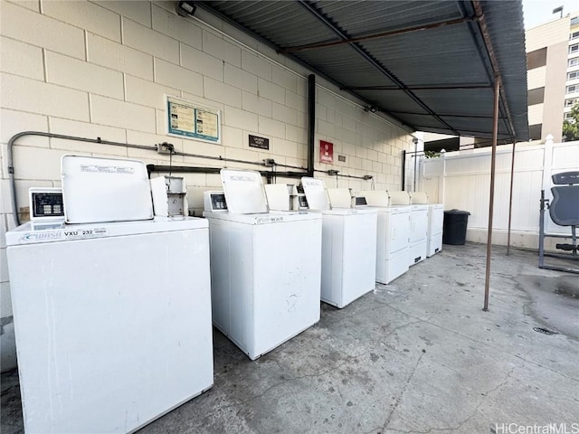 laundry area with concrete block wall, washer and clothes dryer, and community laundry area