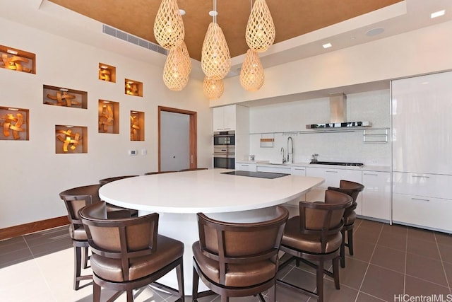 kitchen featuring wall chimney range hood, black stovetop, a tray ceiling, white cabinetry, and dark tile patterned flooring