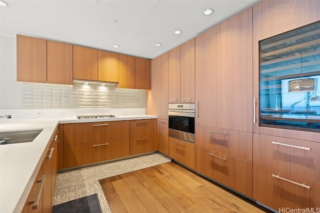 kitchen with a sink, under cabinet range hood, stainless steel appliances, light wood-style floors, and light countertops