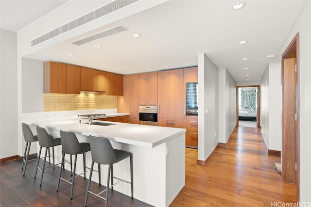 kitchen with oven, light countertops, a peninsula, brown cabinetry, and modern cabinets