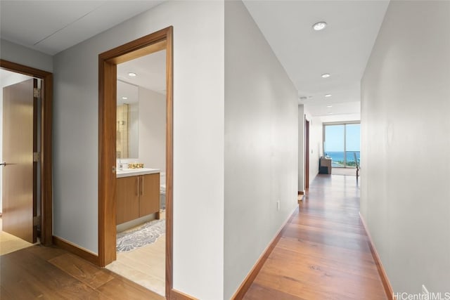 hall featuring light wood-style flooring, recessed lighting, and baseboards