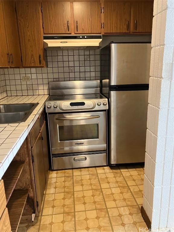 kitchen with stainless steel appliances, decorative backsplash, tile counters, and under cabinet range hood