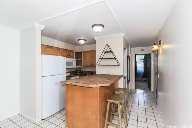 kitchen with a breakfast bar area, light tile patterned flooring, a peninsula, white appliances, and brown cabinets