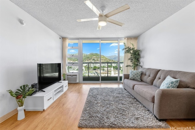 living area featuring a textured ceiling, a wall of windows, light wood-style flooring, and ceiling fan