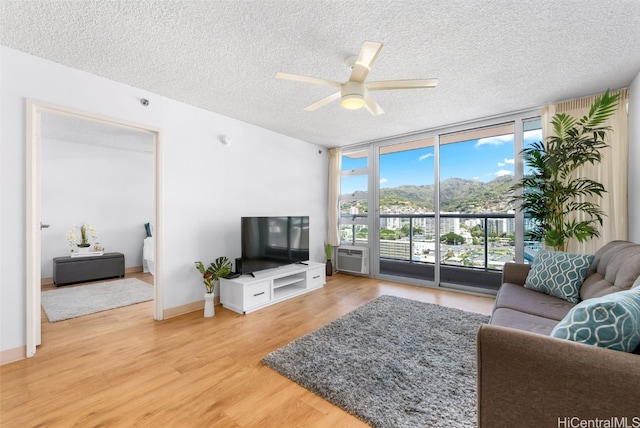 living area featuring a textured ceiling, light wood finished floors, a wall of windows, baseboards, and ceiling fan