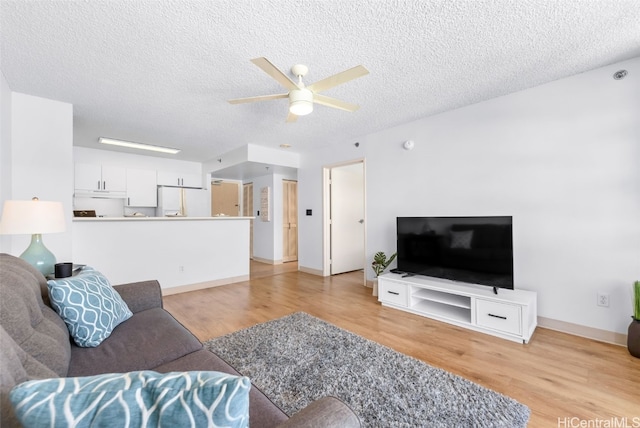 living area featuring a ceiling fan, baseboards, light wood finished floors, and a textured ceiling