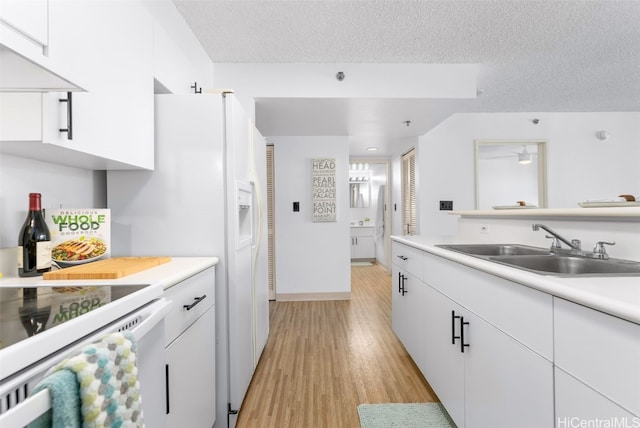 kitchen with light wood finished floors, a textured ceiling, white cabinetry, and a sink