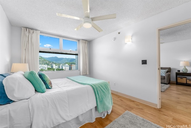 bedroom with light wood-type flooring, baseboards, a textured ceiling, and ceiling fan