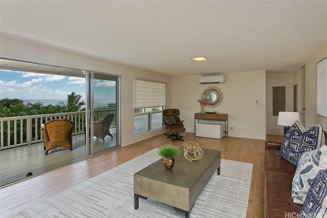 living room featuring an AC wall unit, wood finished floors, and a textured ceiling