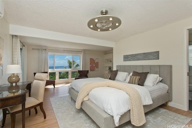 bedroom with light wood finished floors, a textured ceiling, and baseboards