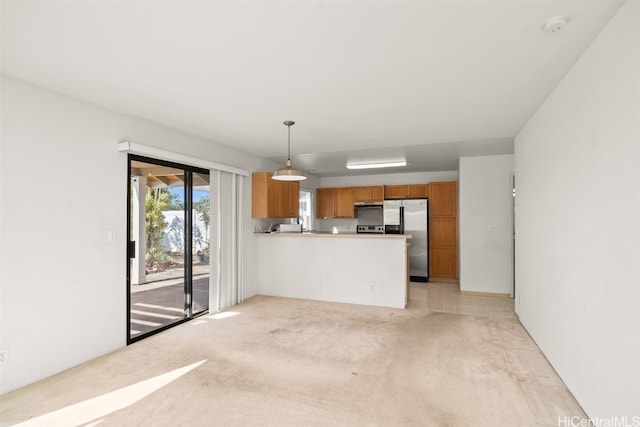 kitchen with light countertops, brown cabinets, a peninsula, hanging light fixtures, and stainless steel fridge