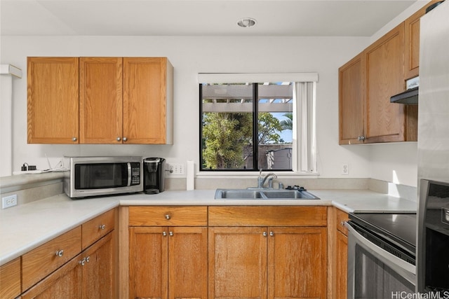 kitchen with brown cabinetry, a sink, stainless steel appliances, light countertops, and under cabinet range hood