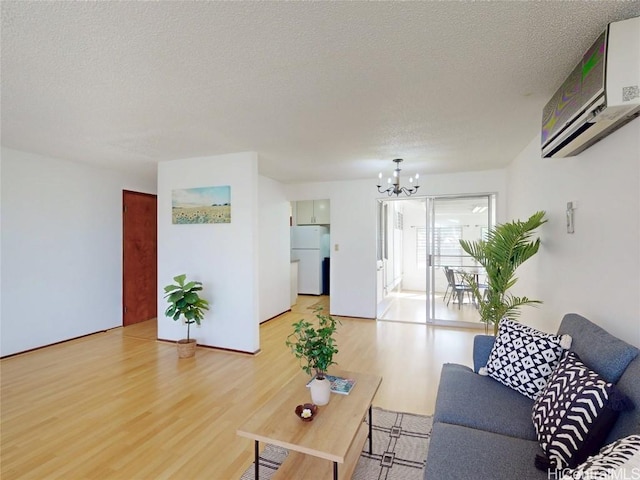 living room featuring light wood finished floors, an inviting chandelier, a textured ceiling, and a wall mounted air conditioner