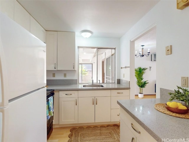 kitchen featuring a chandelier, stove, freestanding refrigerator, white cabinetry, and a sink