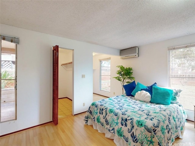 bedroom featuring a walk in closet, wood finished floors, a textured ceiling, and a wall mounted AC