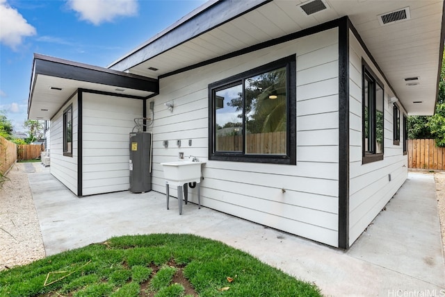 view of property exterior featuring a patio area, water heater, fence, and a sink