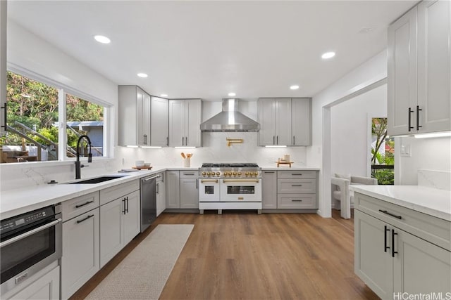 kitchen featuring a sink, light countertops, wall chimney range hood, appliances with stainless steel finishes, and backsplash