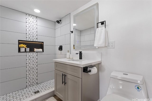 full bath with vanity, a tile shower, and toilet