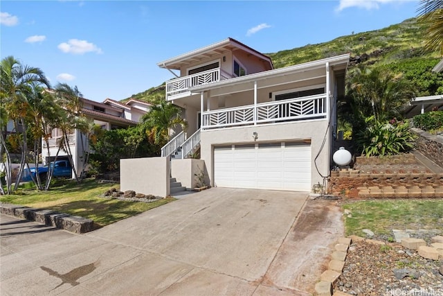 view of front of property featuring stairs, driveway, a balcony, and stucco siding