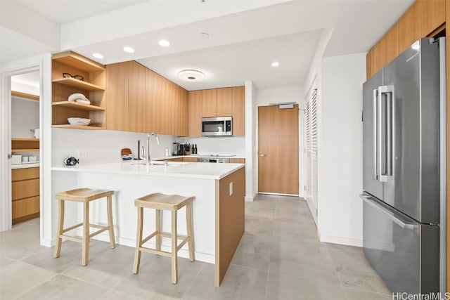 kitchen with a peninsula, a sink, light countertops, appliances with stainless steel finishes, and modern cabinets