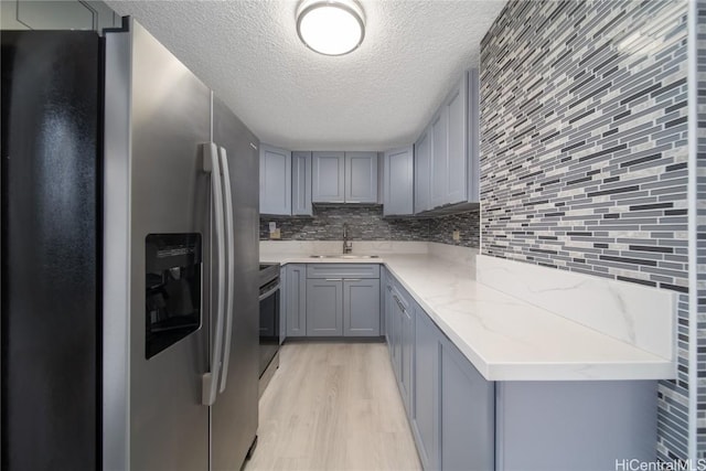 kitchen with gray cabinetry, stainless steel appliances, a sink, backsplash, and light wood finished floors