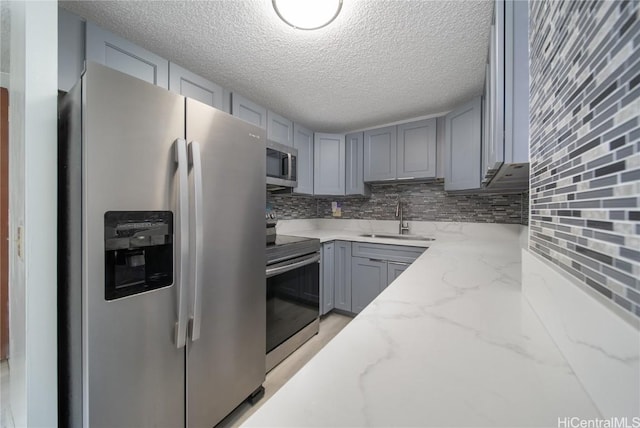 kitchen featuring light stone counters, stainless steel appliances, decorative backsplash, gray cabinetry, and a sink