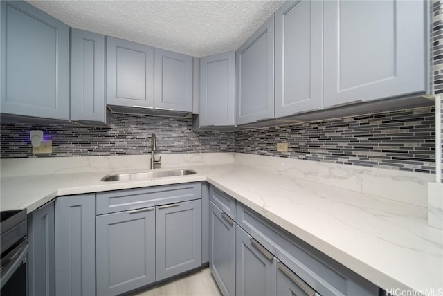 kitchen featuring light stone counters, backsplash, a sink, and gray cabinetry