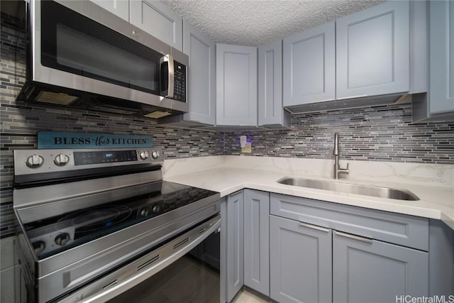 kitchen with stainless steel appliances, a sink, light stone counters, and gray cabinetry