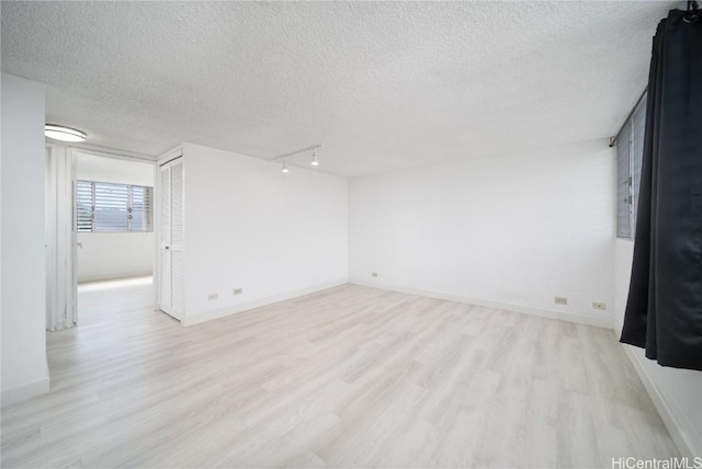 spare room with light wood finished floors, baseboards, and a textured ceiling