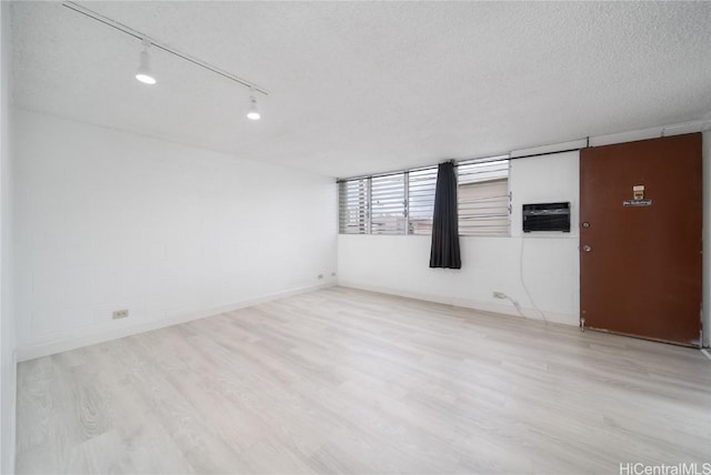 spare room with a textured ceiling, an AC wall unit, wood finished floors, and track lighting