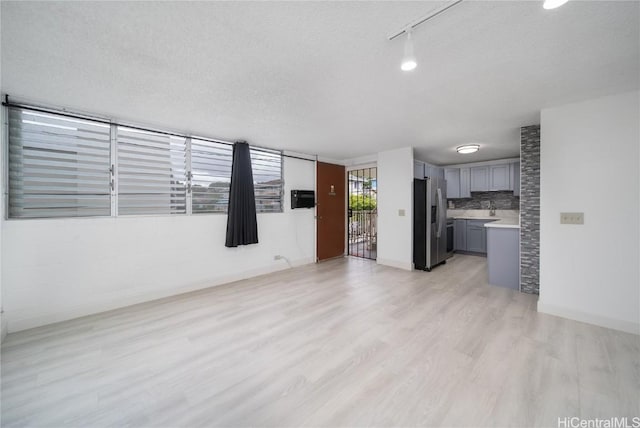 unfurnished living room featuring light wood-type flooring, a textured ceiling, and baseboards