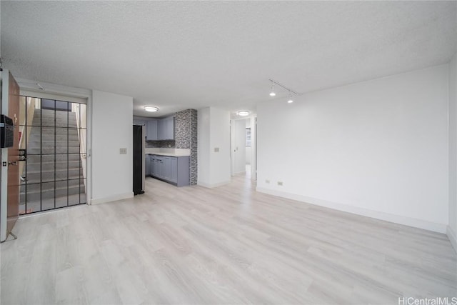 unfurnished living room with light wood-style flooring, baseboards, and a textured ceiling