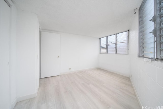 empty room with concrete block wall, light wood finished floors, baseboards, and a textured ceiling