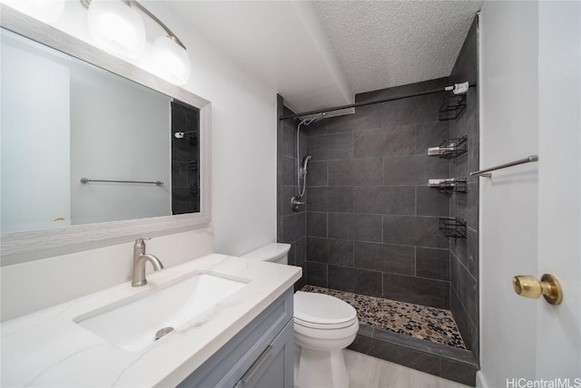 full bathroom featuring toilet, a textured ceiling, tiled shower, and vanity