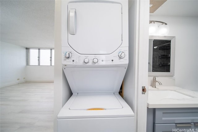 laundry room featuring a textured ceiling, stacked washer and dryer, laundry area, wood finished floors, and a sink