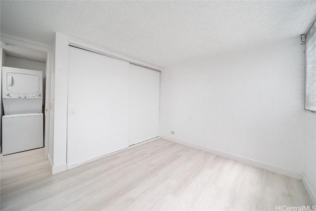 unfurnished bedroom with a textured ceiling, stacked washer / dryer, a closet, and light wood-style floors