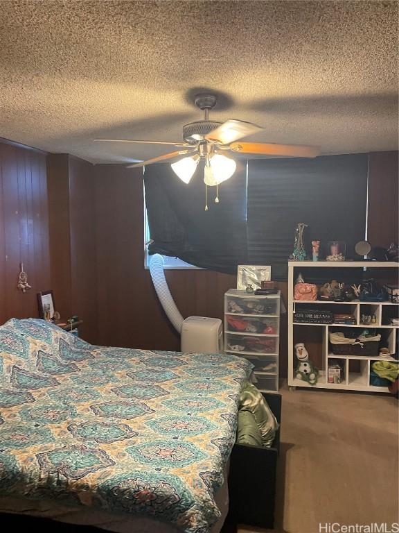 bedroom featuring a textured ceiling, ceiling fan, and wooden walls