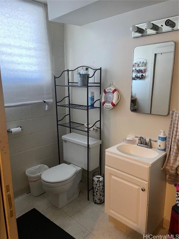 half bathroom featuring tile walls, vanity, toilet, and tile patterned floors