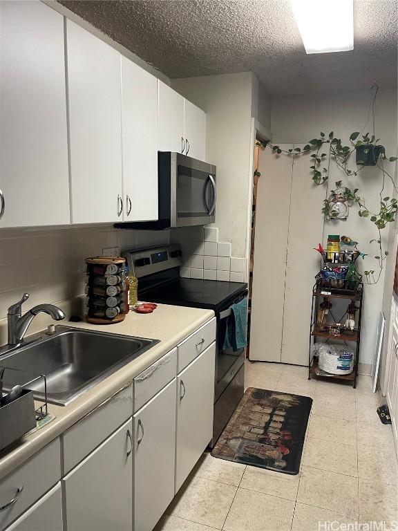 kitchen with stainless steel appliances, a sink, white cabinetry, light countertops, and decorative backsplash