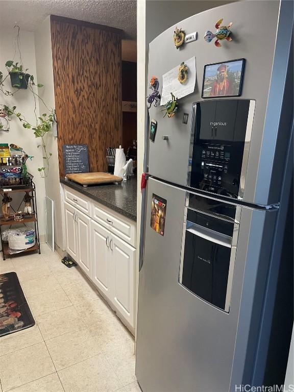 kitchen with light tile patterned floors, white cabinets, dark countertops, freestanding refrigerator, and a textured ceiling