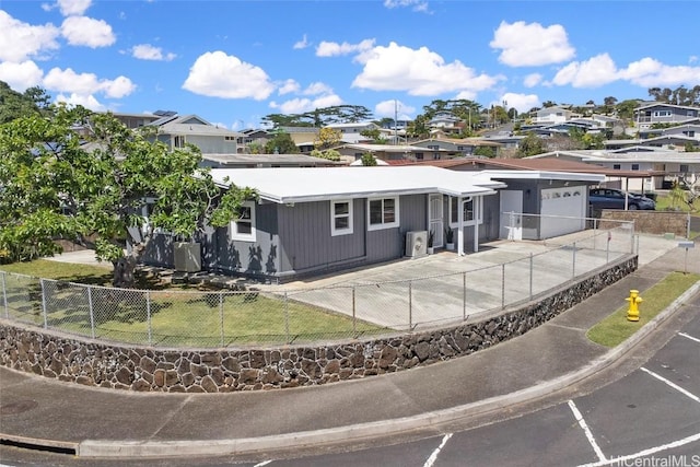 rear view of house featuring a fenced front yard, a yard, concrete driveway, an attached garage, and a residential view