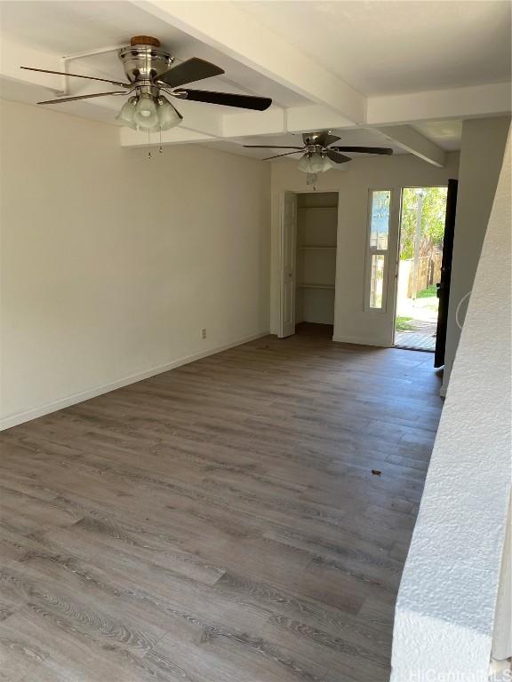 spare room featuring beamed ceiling, wood finished floors, a ceiling fan, and baseboards