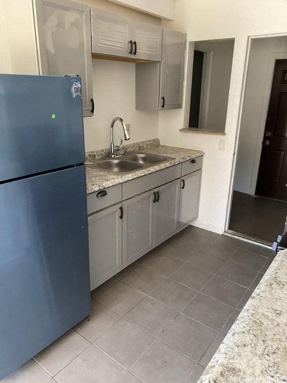 kitchen with light countertops, freestanding refrigerator, tile patterned flooring, and a sink